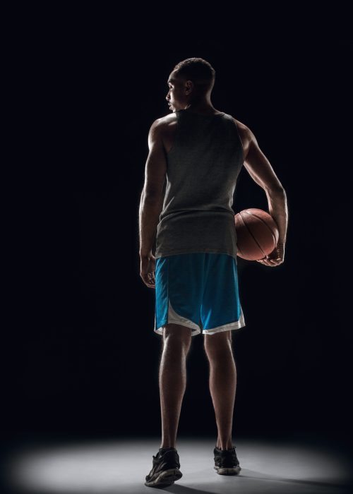 The portrait of a basketball player with a ball against dark studio background. advertising concept